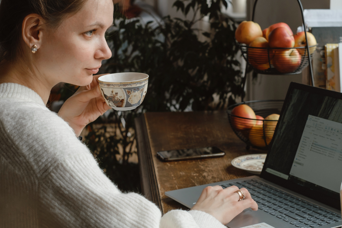 Woman enjoying tea while working on a laptop, surrounded by autumn decor and a cozy atmosphere