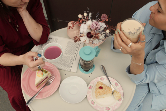 Friends enjoying tea with cakes, tea, and flowers on a pastel table.