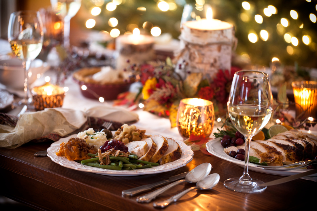 Warm holiday dinner table set with festive food, candles, and wine glasses.