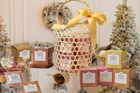 Mala Tara holiday tea products arranged with woven basket, ornaments, and Christmas trees.