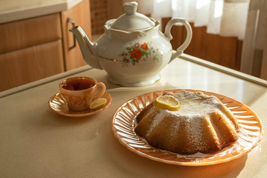 Floral teapot and teacup served with a lemon bundt cake on a peach plate by a sunny window.
